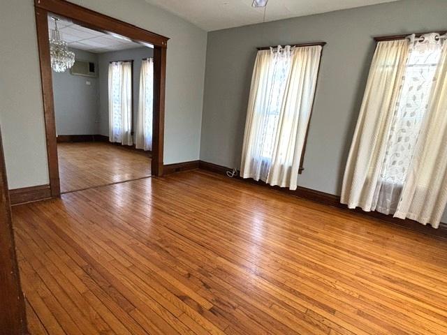 empty room featuring a notable chandelier, wood finished floors, a wealth of natural light, and baseboards