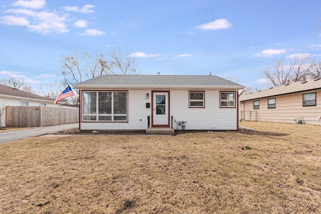 view of front of house with a shingled roof, a front yard, and fence