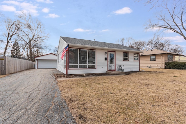 view of front of property with an outbuilding, a garage, a shingled roof, fence, and a front lawn