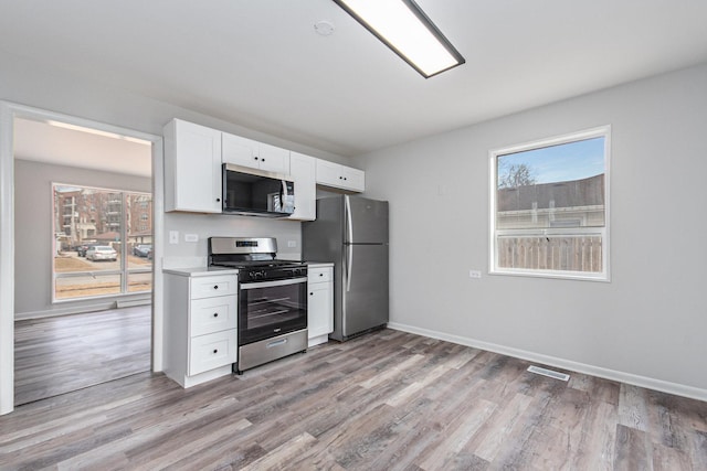 kitchen featuring light wood-style flooring, stainless steel appliances, white cabinetry, baseboards, and light countertops