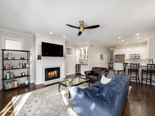 living room with dark wood-style floors, wine cooler, a glass covered fireplace, and ornamental molding