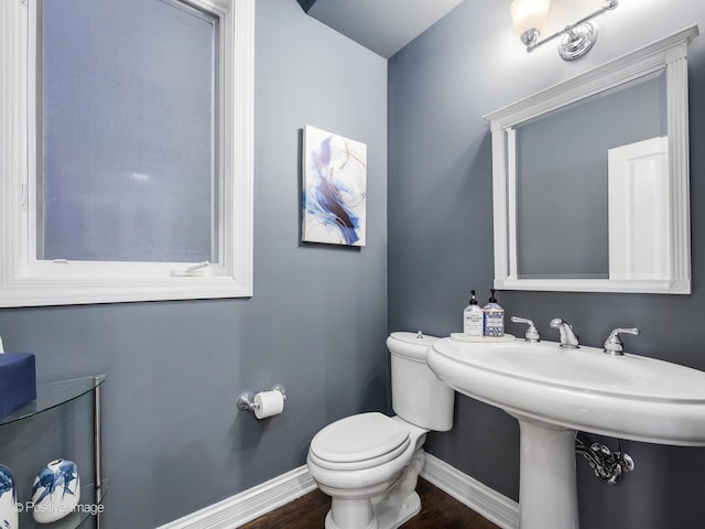 half bathroom with wood finished floors, toilet, and baseboards