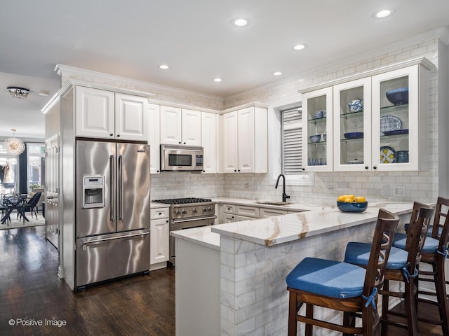 kitchen with white cabinets, a sink, a peninsula, and high quality appliances