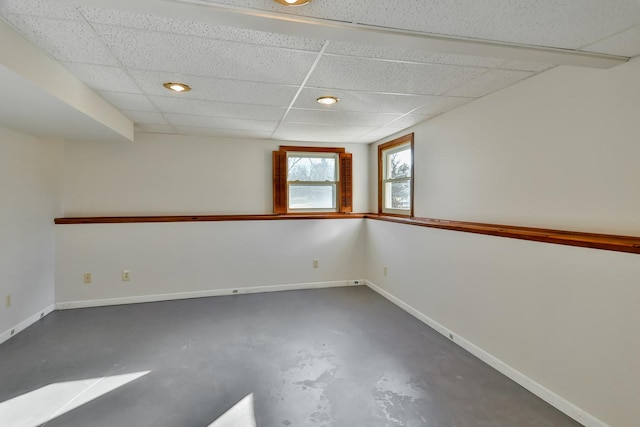 basement with a paneled ceiling and baseboards