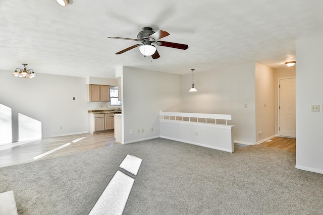 unfurnished living room with baseboards, ceiling fan with notable chandelier, and light colored carpet