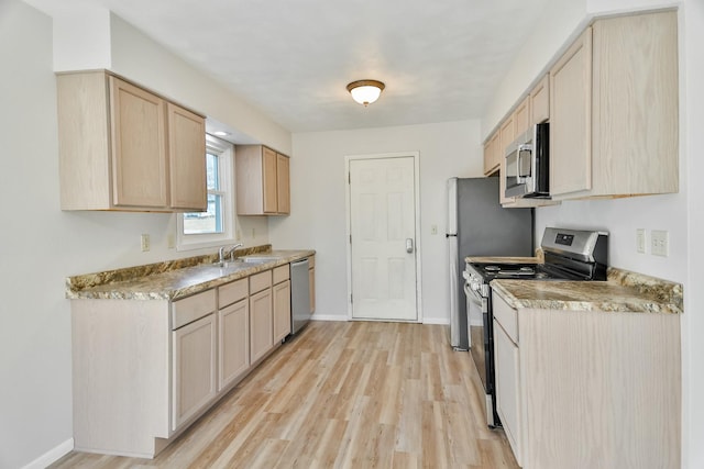 kitchen with stainless steel appliances, light brown cabinets, a sink, light wood-type flooring, and baseboards