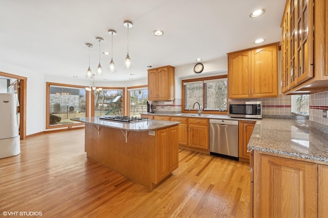 kitchen featuring decorative backsplash, light wood-style flooring, appliances with stainless steel finishes, a center island, and a sink