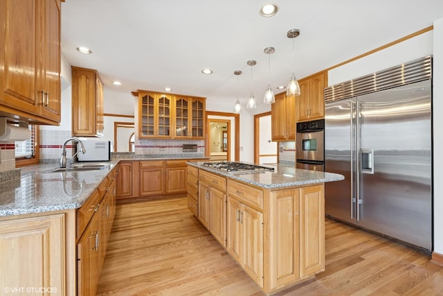 kitchen with light wood-type flooring, a kitchen island, appliances with stainless steel finishes, and glass insert cabinets