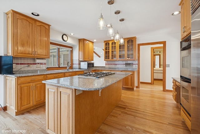 kitchen featuring appliances with stainless steel finishes, light wood-style floors, glass insert cabinets, a sink, and a kitchen island