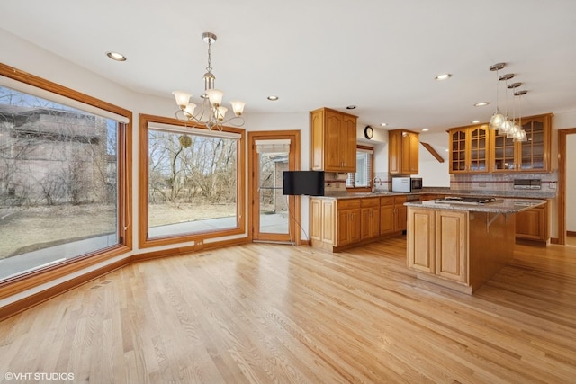 kitchen featuring a center island, light wood-style flooring, an inviting chandelier, glass insert cabinets, and a sink