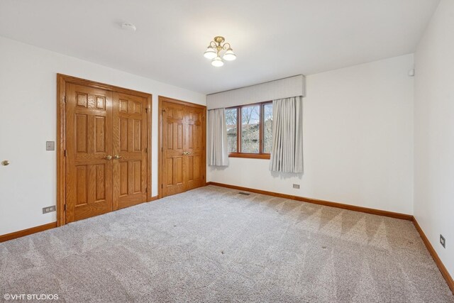 unfurnished bedroom with carpet flooring, visible vents, baseboards, and two closets