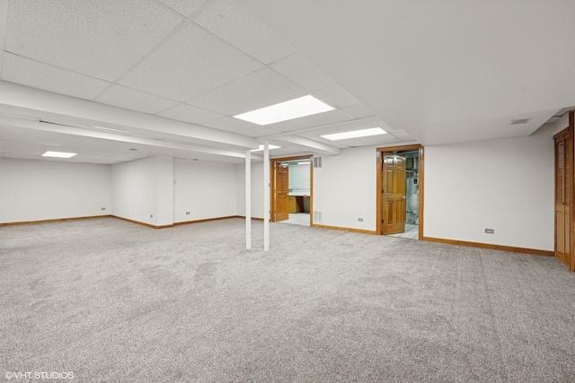 finished below grade area with light carpet, visible vents, a paneled ceiling, and baseboards