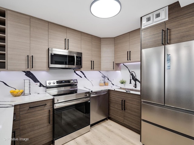 kitchen with light wood-style floors, appliances with stainless steel finishes, light countertops, and a sink