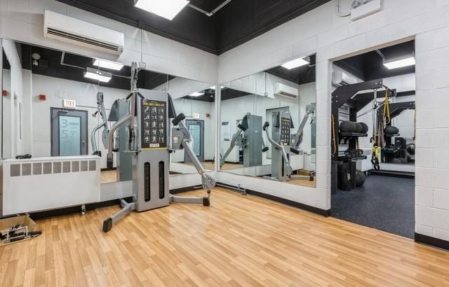 gym with a wall unit AC, wood finished floors, concrete block wall, and radiator