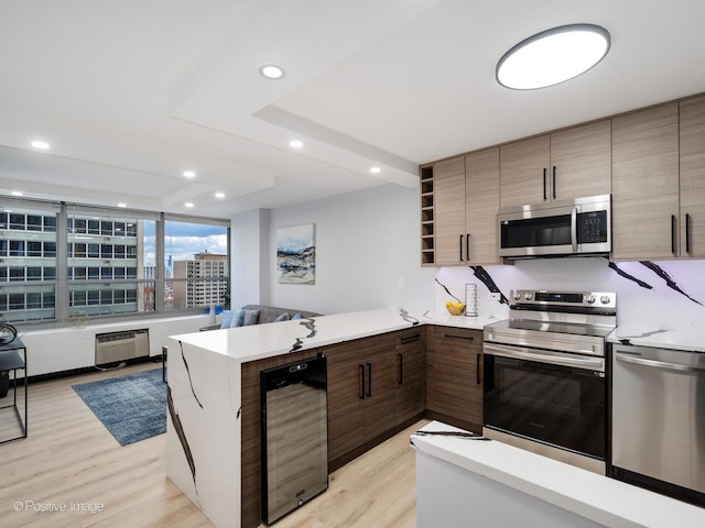 kitchen featuring stainless steel appliances, a peninsula, open floor plan, light countertops, and modern cabinets