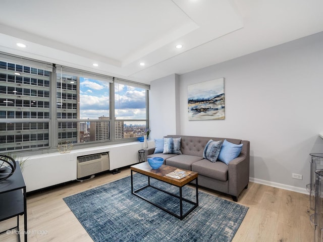 living room featuring light wood-style flooring, baseboards, a raised ceiling, and recessed lighting