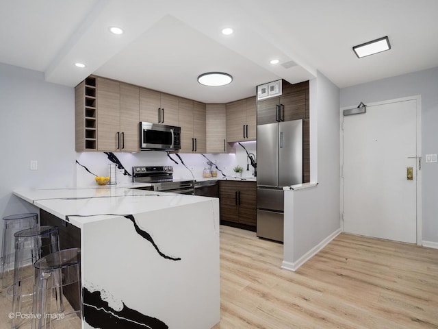 kitchen with a peninsula, a breakfast bar, appliances with stainless steel finishes, open shelves, and light wood finished floors