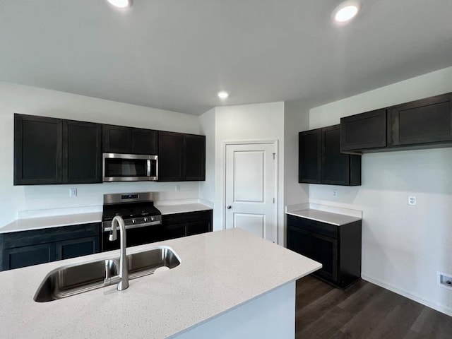 kitchen with dark wood finished floors, dark cabinetry, stainless steel appliances, and a sink