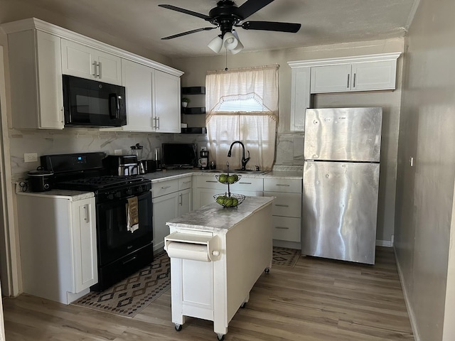 kitchen featuring light wood-type flooring, black appliances, white cabinetry, and a sink