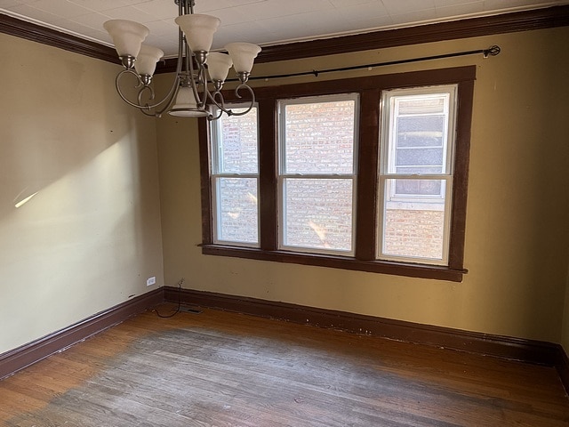 unfurnished dining area featuring crown molding, baseboards, wood finished floors, and a notable chandelier