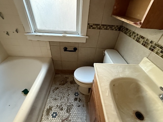 bathroom featuring tile patterned flooring, toilet, a sink, tile walls, and a bath