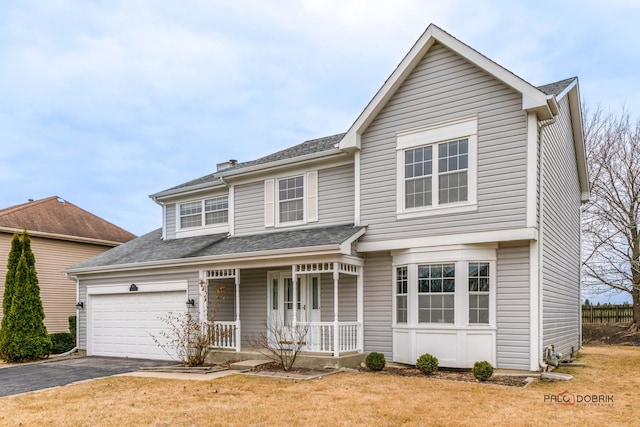 traditional-style home featuring an attached garage, covered porch, a front lawn, and aphalt driveway