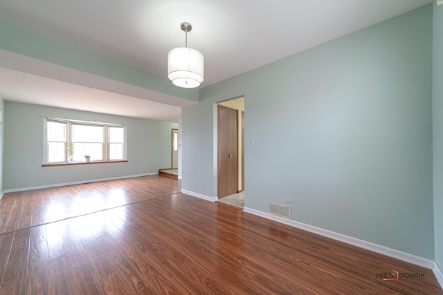 spare room featuring wood finished floors, visible vents, and baseboards