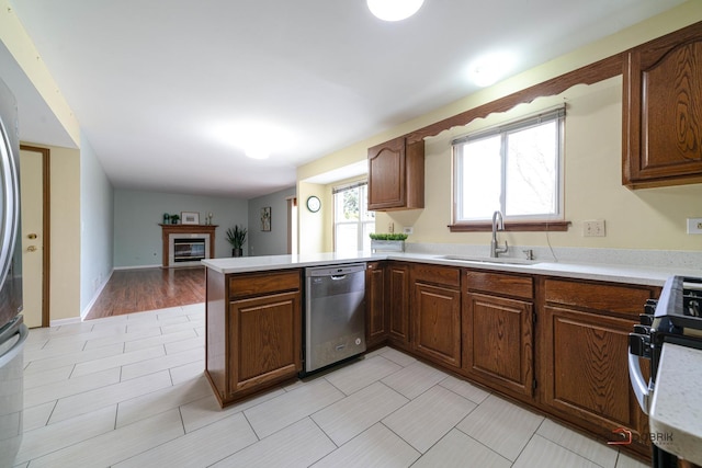 kitchen featuring range with gas stovetop, dishwasher, a glass covered fireplace, a peninsula, and a sink