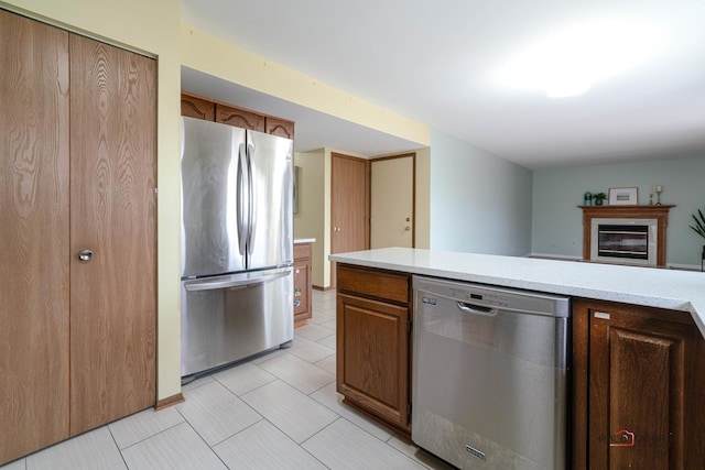 kitchen with appliances with stainless steel finishes, a glass covered fireplace, brown cabinets, and light countertops