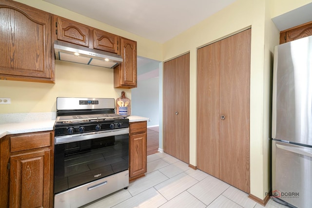 kitchen with stainless steel appliances, brown cabinetry, light countertops, and under cabinet range hood