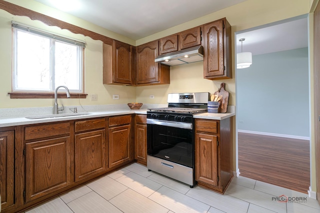 kitchen featuring light countertops, stainless steel gas stove, a sink, and under cabinet range hood