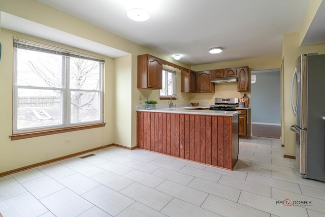 kitchen featuring under cabinet range hood, a peninsula, a sink, visible vents, and appliances with stainless steel finishes