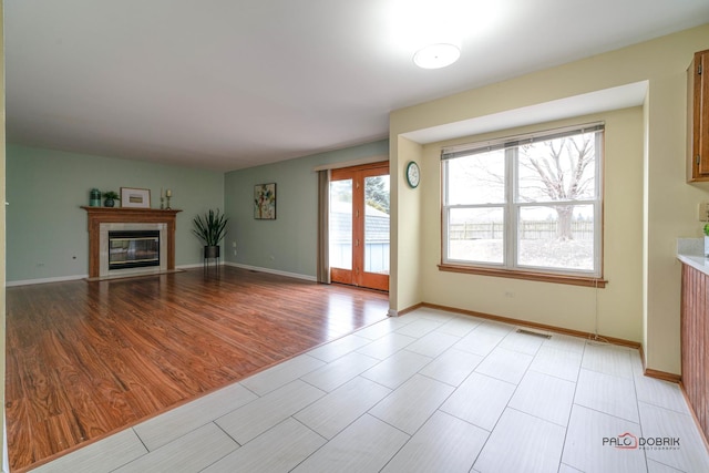 unfurnished living room with light wood-style flooring, visible vents, baseboards, and a glass covered fireplace