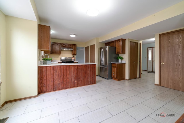 kitchen featuring a peninsula, under cabinet range hood, appliances with stainless steel finishes, and light countertops