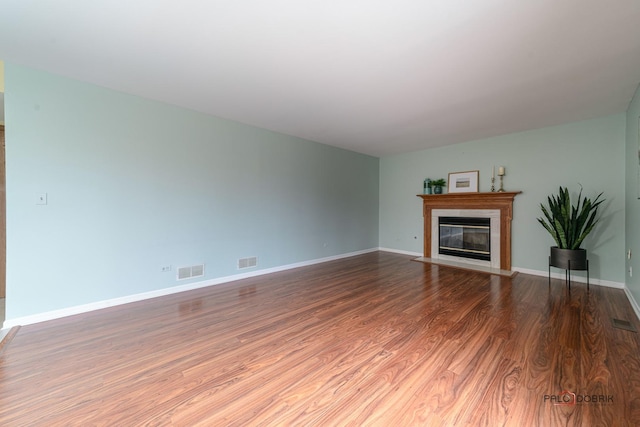 unfurnished living room featuring baseboards, a fireplace with flush hearth, visible vents, and wood finished floors