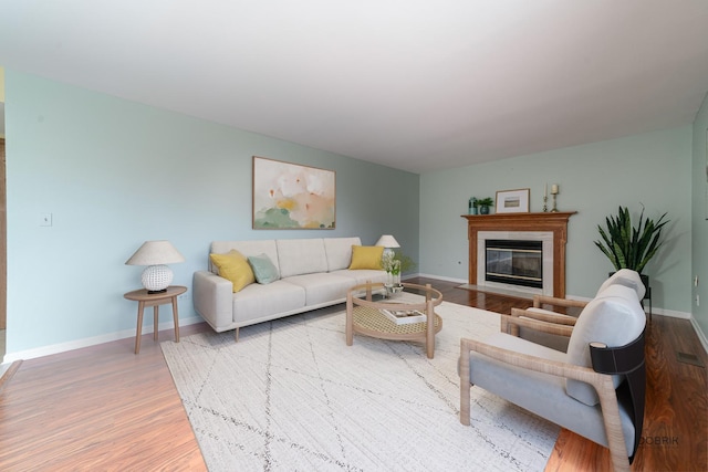 living area featuring a fireplace with flush hearth, wood finished floors, and baseboards