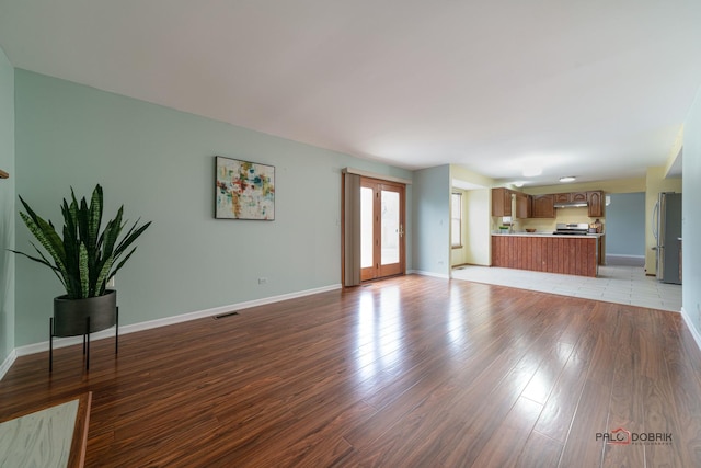 unfurnished living room with light wood finished floors, baseboards, visible vents, and french doors