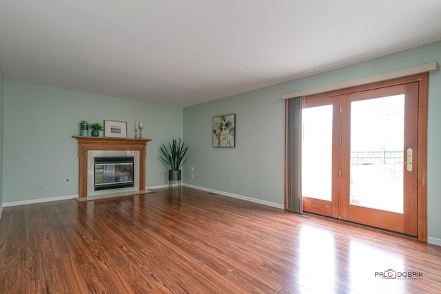 unfurnished living room with wood finished floors, a fireplace with flush hearth, and baseboards