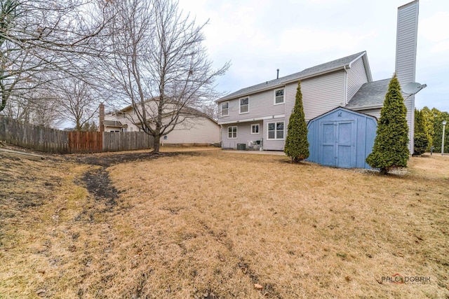 rear view of house featuring a yard, a chimney, a storage shed, fence, and an outdoor structure