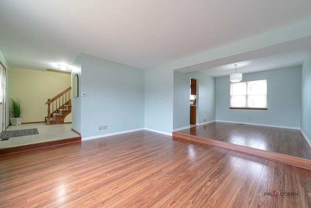 unfurnished living room featuring stairs, hardwood / wood-style flooring, visible vents, and baseboards