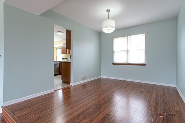 unfurnished room featuring dark wood-type flooring, visible vents, and baseboards