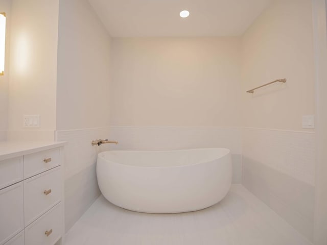 bathroom with wainscoting, a soaking tub, vanity, and tile walls