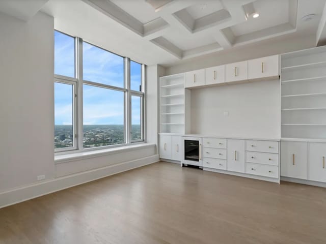 unfurnished living room with beverage cooler, coffered ceiling, light wood-style flooring, and baseboards