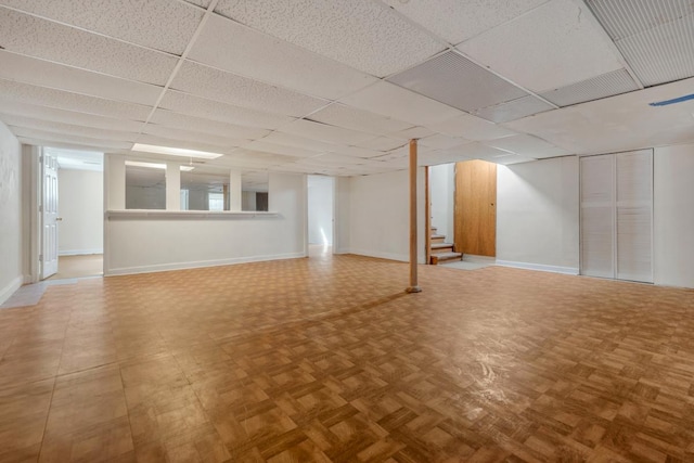 finished basement with a paneled ceiling, stairway, and baseboards