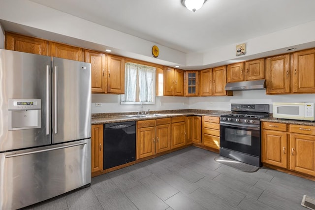 kitchen with under cabinet range hood, stainless steel appliances, a sink, brown cabinets, and dark countertops