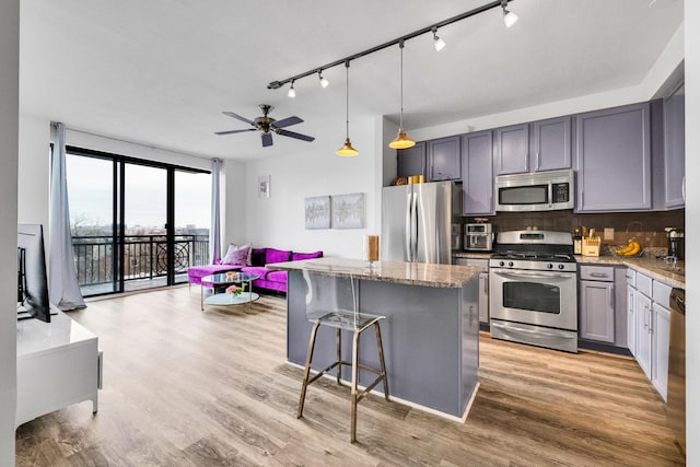 kitchen with a kitchen island, appliances with stainless steel finishes, light stone countertops, light wood finished floors, and tasteful backsplash