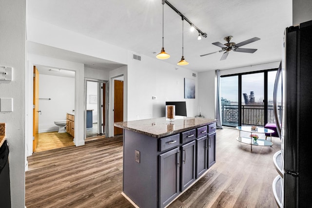 kitchen with stone countertops, visible vents, hanging light fixtures, freestanding refrigerator, and dark wood finished floors