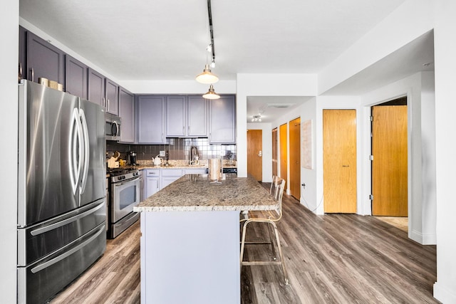 kitchen with tasteful backsplash, appliances with stainless steel finishes, a kitchen breakfast bar, wood finished floors, and light stone countertops