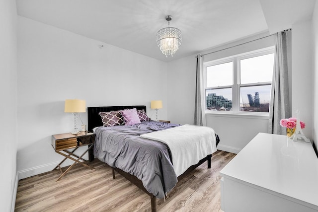 bedroom featuring light wood finished floors, baseboards, and a notable chandelier