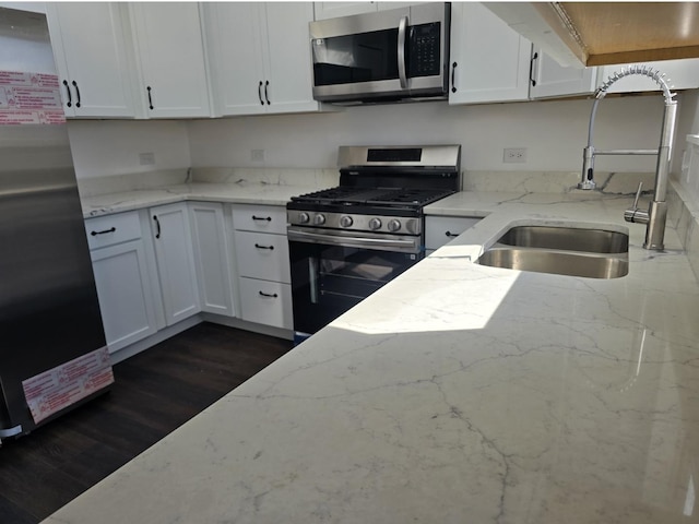 kitchen with dark wood-type flooring, a sink, white cabinetry, appliances with stainless steel finishes, and light stone countertops